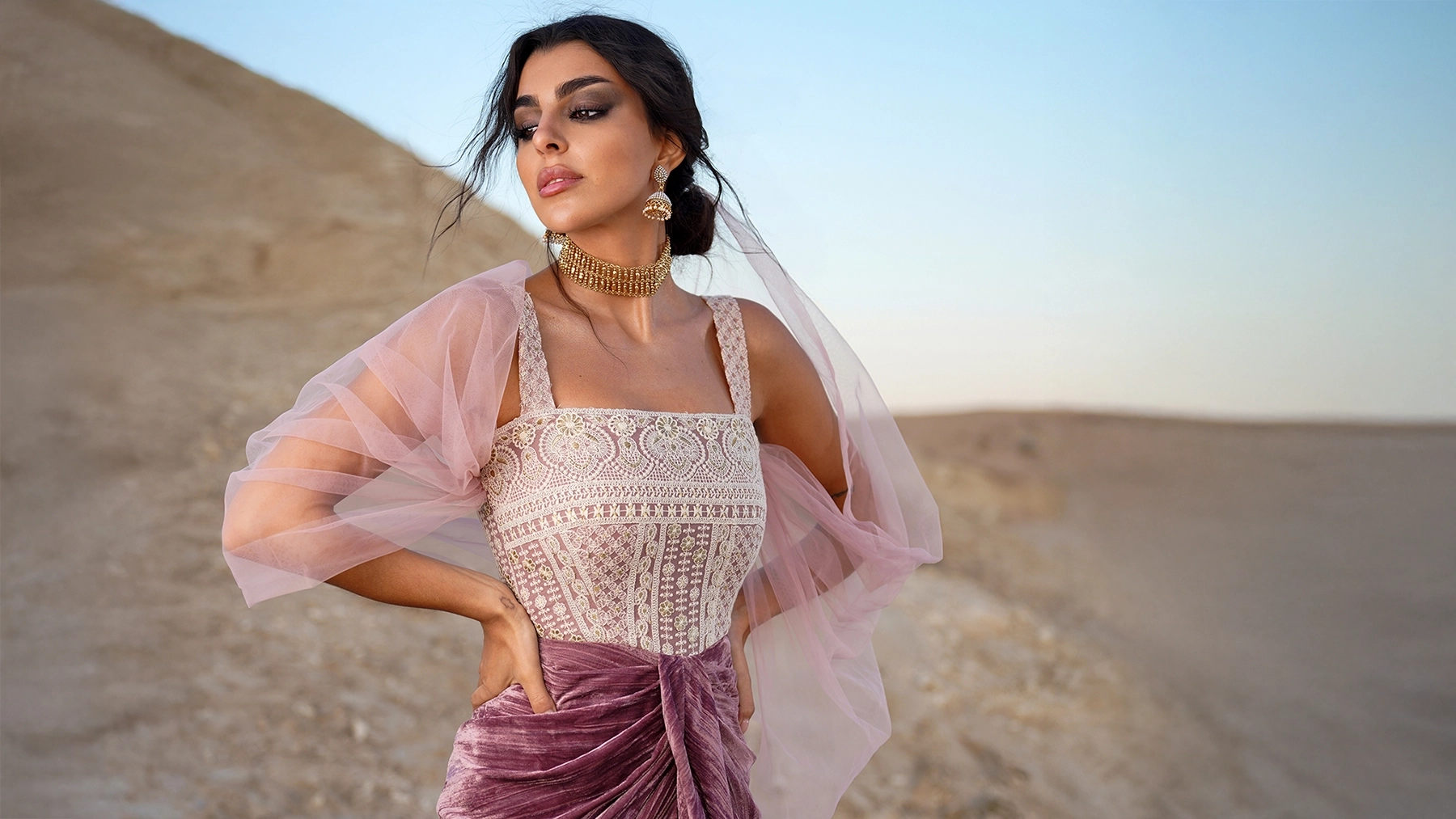 Model in an editorial desert fashion shoot wearing a lace bodice, pink draped skirt, and gold jewelry by Studio LeTouch