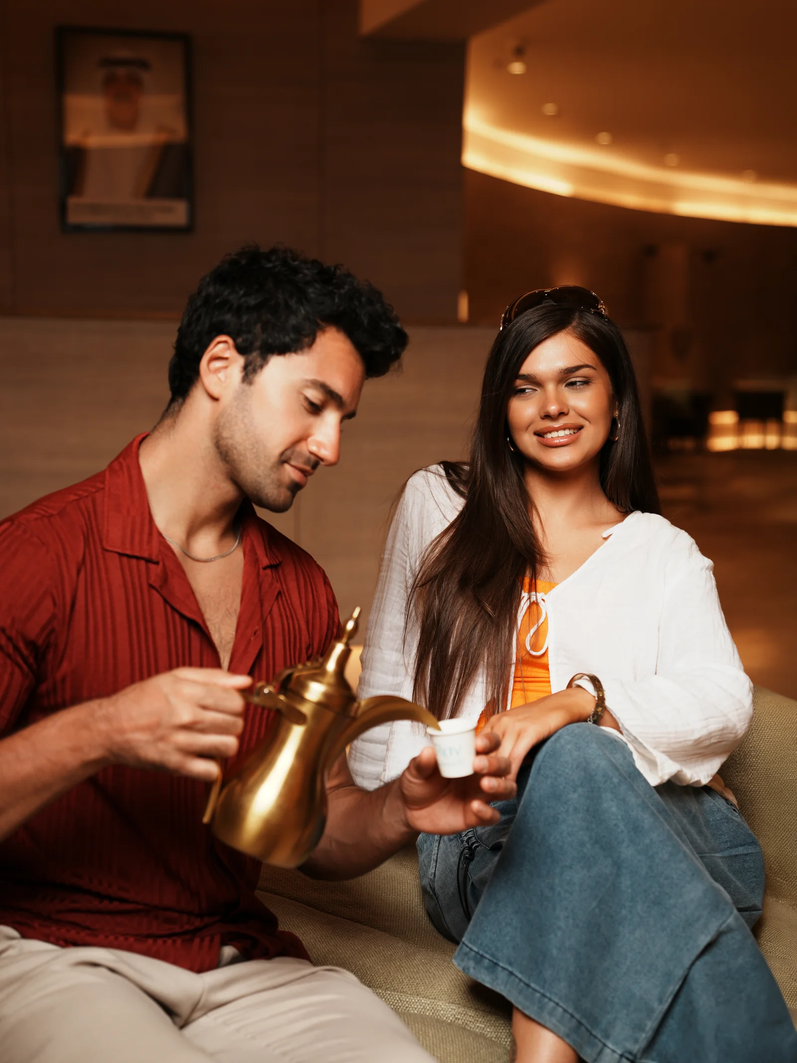 Man pouring Arabic coffee from a brass dallah for a woman in the lounge at RAY Hotel Kuwait